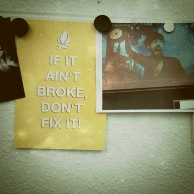 An einer Metallleiste, die an einer Wand befestigt ist, sind mit kleinen Magneten Zettel angeheftet, auf denen jemand Memes ausgedruckt hat. Erkennbar sind zwei: „If it ain't broke, don't fix it“ und ein Filmstill aus „Das Boot“