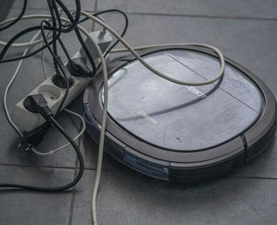 Ein Roboter-Staubsauger hat sich neben einer Mehrfachsteckdose im Kabelsalat festgefahren.