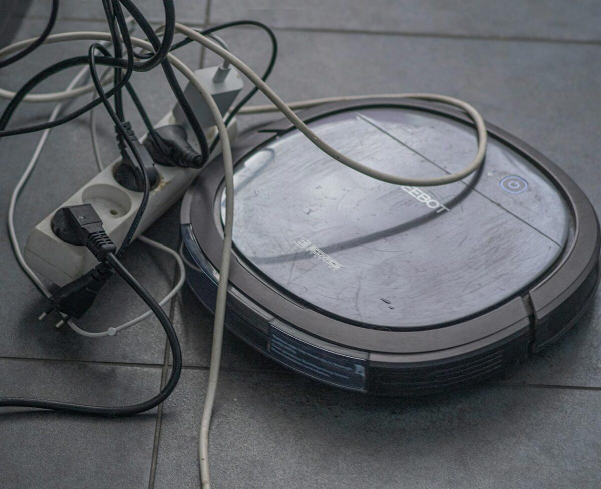 Ein Roboter-Staubsauger hat sich neben einer Mehrfachsteckdose im Kabelsalat festgefahren.
