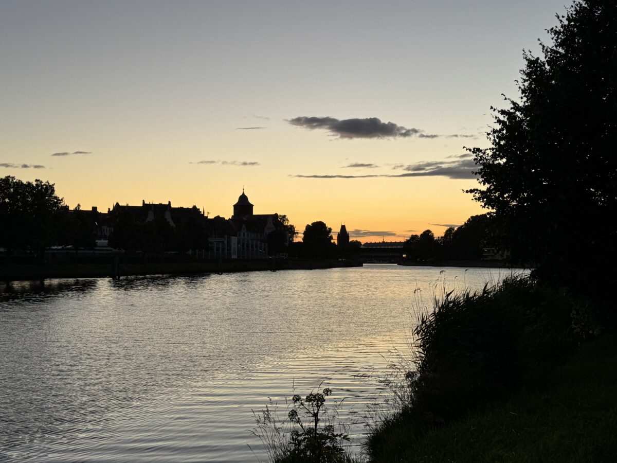 Sonnenuntergangsszene am Lübecker Klughafen. Im Vordergrund der Elbe-Lübeck-Kanal, im Hintergrund eine Brücke und die Silhouette des Burgtors.