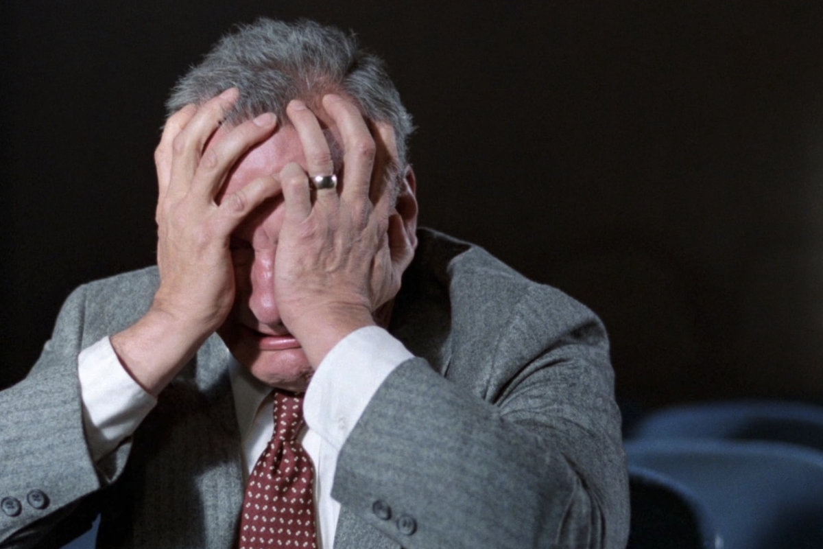 Filmstill aus Hardcore 1979. George C. Scott sitzt in einem leeren Kinosaal und hält sich in aller Verzweiflung die Hände vor das Gesicht. Er weint.