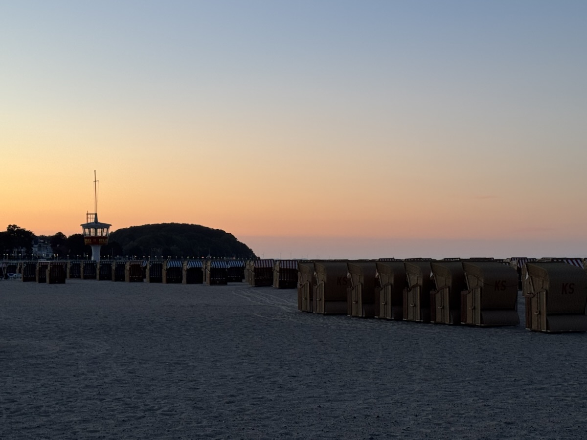 Strand von Travemünde zum Sonnenuntergang. Vorne endlose Reihen Strandkörbe, im Hintergrund das Brodtener Ufer