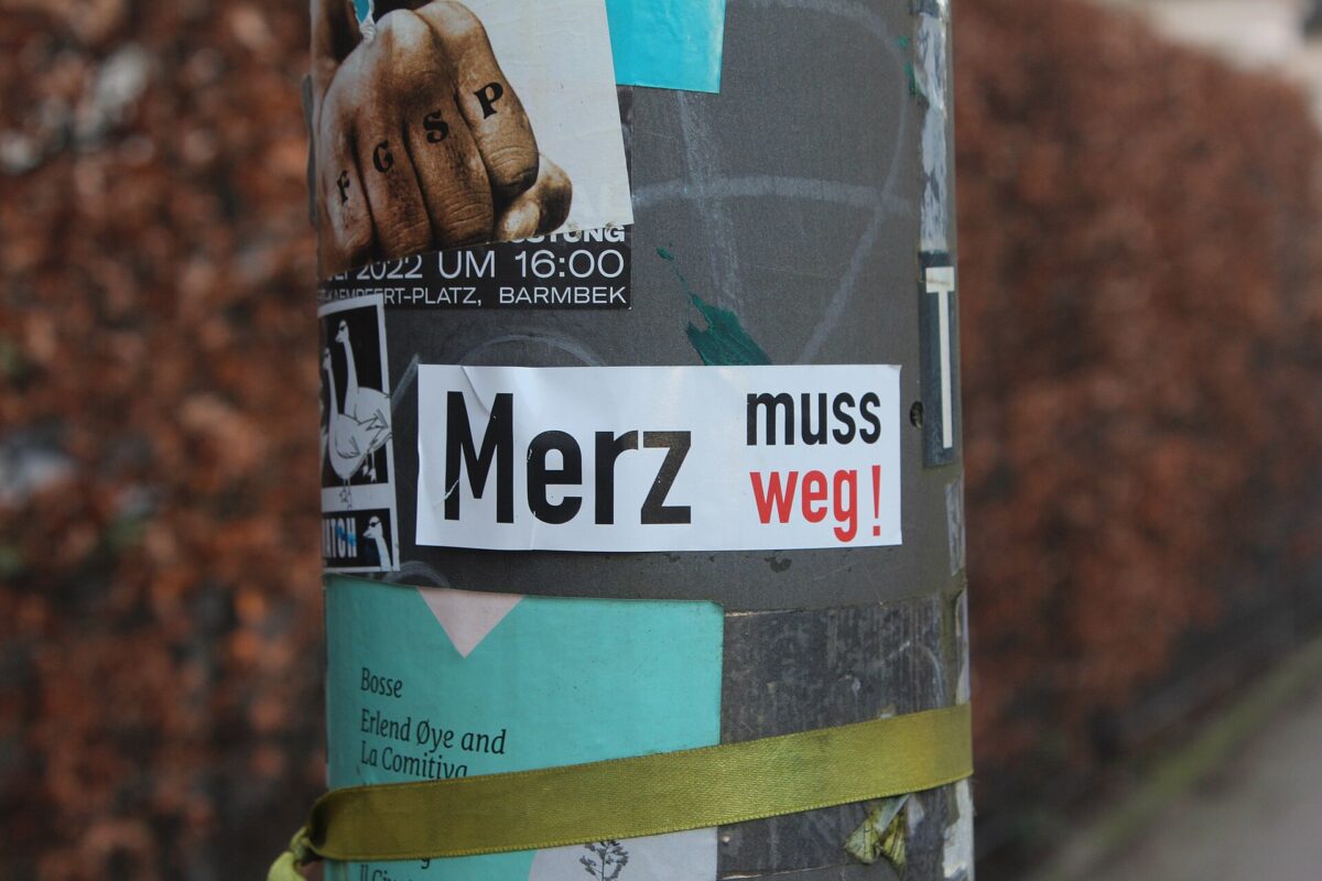 Laternenpfahl mit Aufklebern, in der Mitte ein Aufkleber: „Merz muss weg“