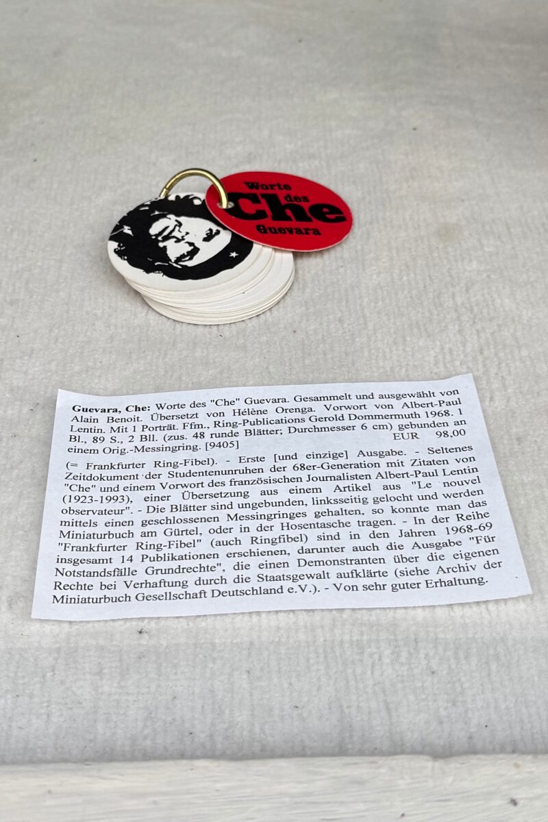 In der Auslage eines Antiquariats liegt auf hellem Teppichstoff ein kleines Büchlein, das aus kreisrunden Seiten besteht von ca. 6cm Durchmesser, die von einem Messingring zusammengehalten werden. Der Titel „Worte des Che Guevara“.