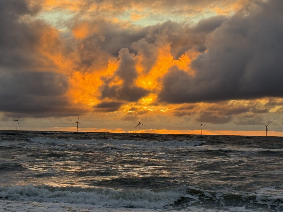 Sonnenuntergang über der Nordsee, im Hintergrund Windräder auf See.