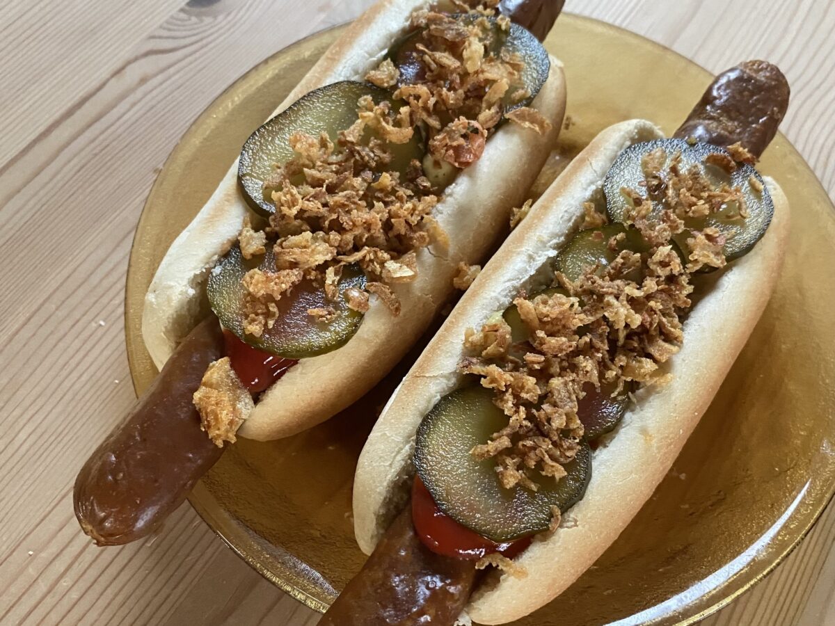 Zwei reichlich belegte Hot Dog auf einem Glasteller auf einem Holztisch